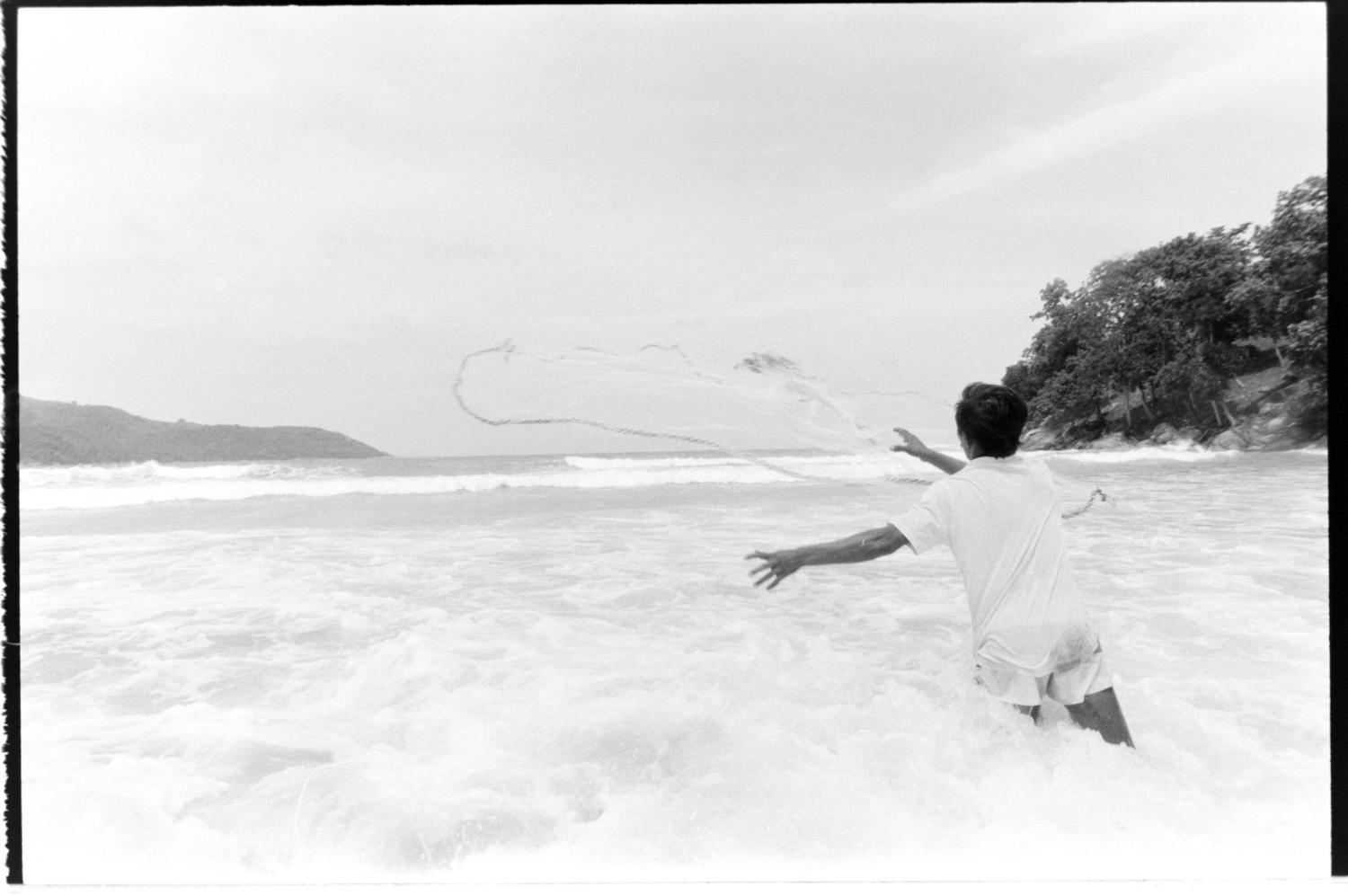 A fisherman casting his net into the sea, from the shallows.